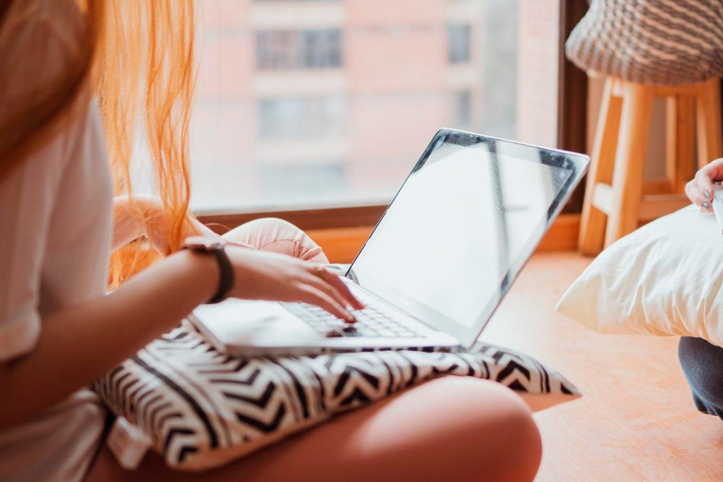 girl typing on laptop with pillow on her lap